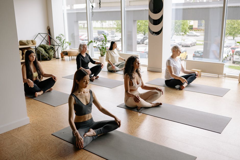Diverse group of people smiling and sitting on yoga mats in a modern studio.